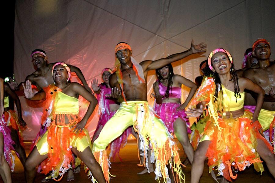 Varias parejas bailando mapalé en escena con trajes naranja y morados