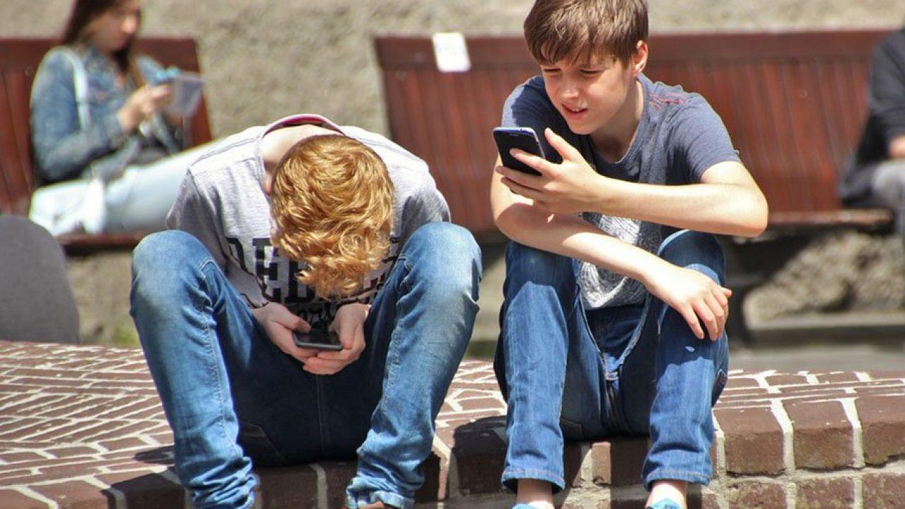 Dos chicos sentados viendo sus celulares.