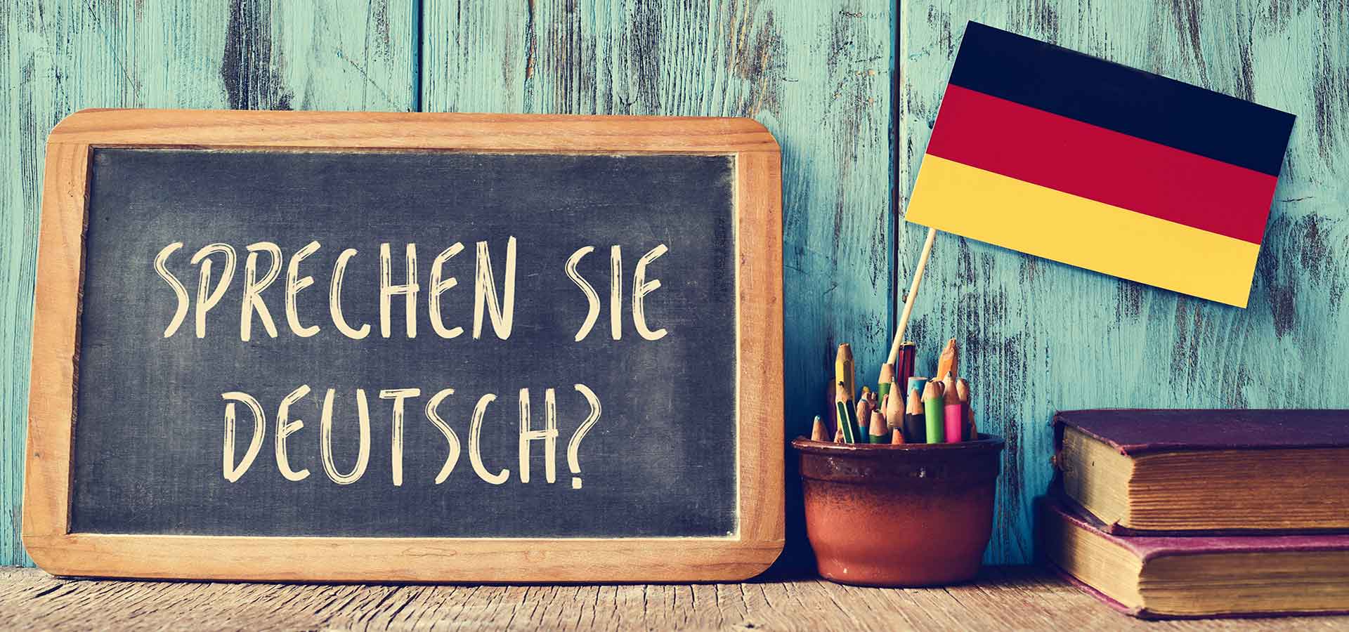 Bandera de Alemania entre caja de lápices, y una pizarra con el letrero en alemán que dice: Sprechen sie deutsch? ¿Hablas alemán?