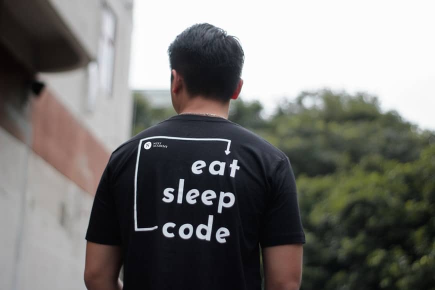 Hombre de espaldas mostrando el letrero de su camiseta que dice: Eat sleep code