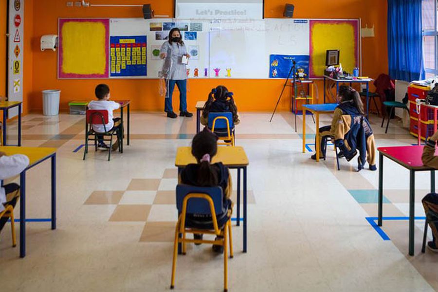 Niños en un salón de clases, prestando atención a su profesora que explica un tema desde el pizarrón.