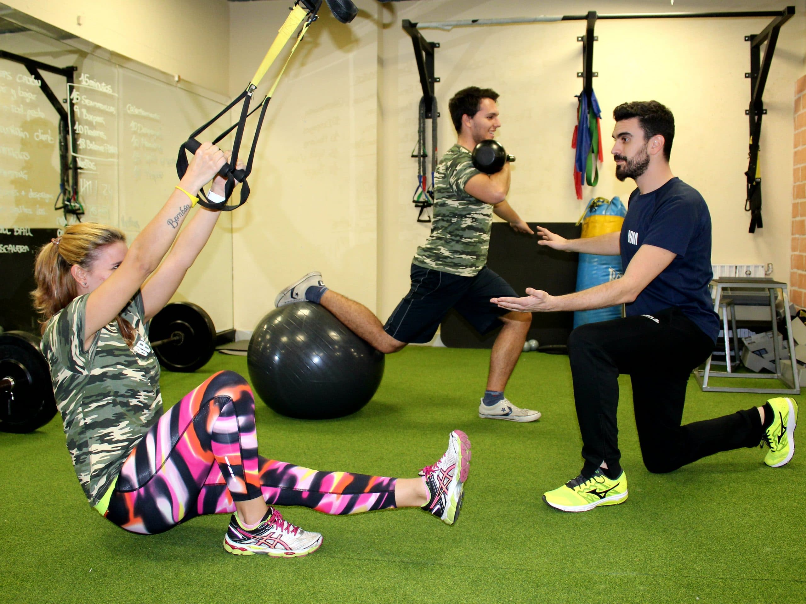 Entrenador acompañando la rutina de dos de sus clientes.