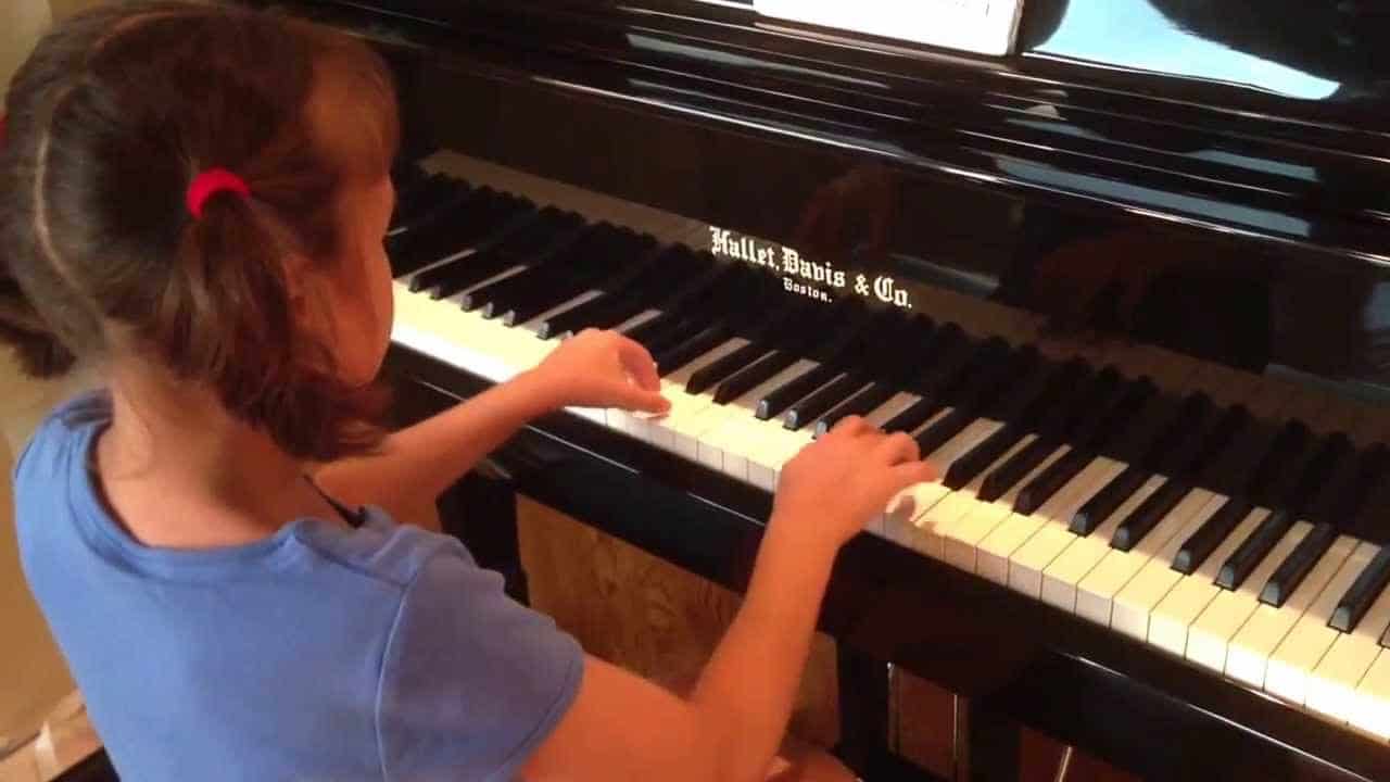 Niña con sus manos puestas en teclado del piano.