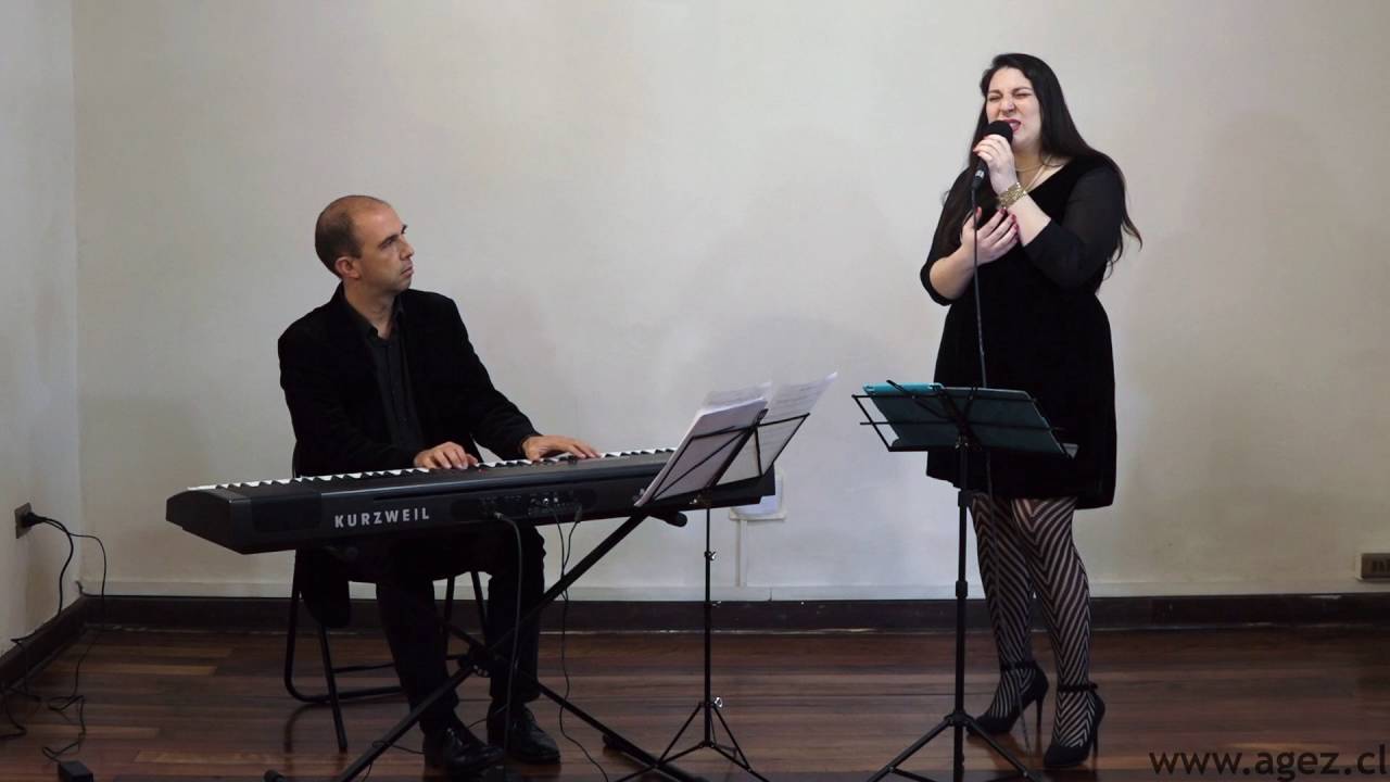 Chico sentado tocando un teclado, mientras una mujer que está de pie canta.