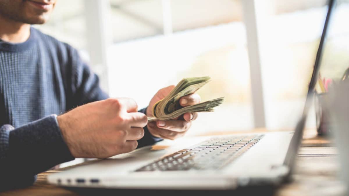 Chico sentado frente a su pc, contando dinero.