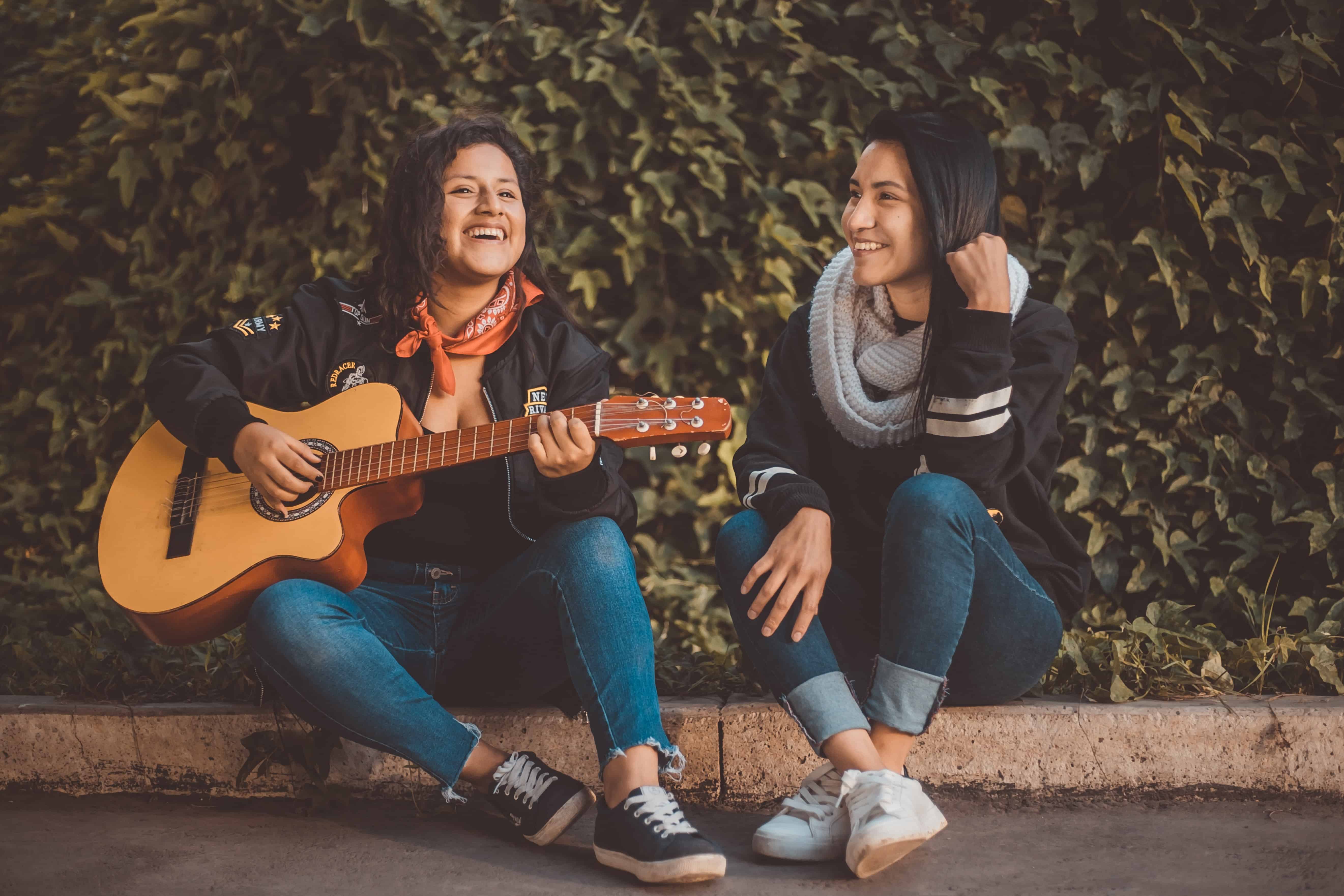 Chicas sentadas en un andén tocando guitarra y sonriendo