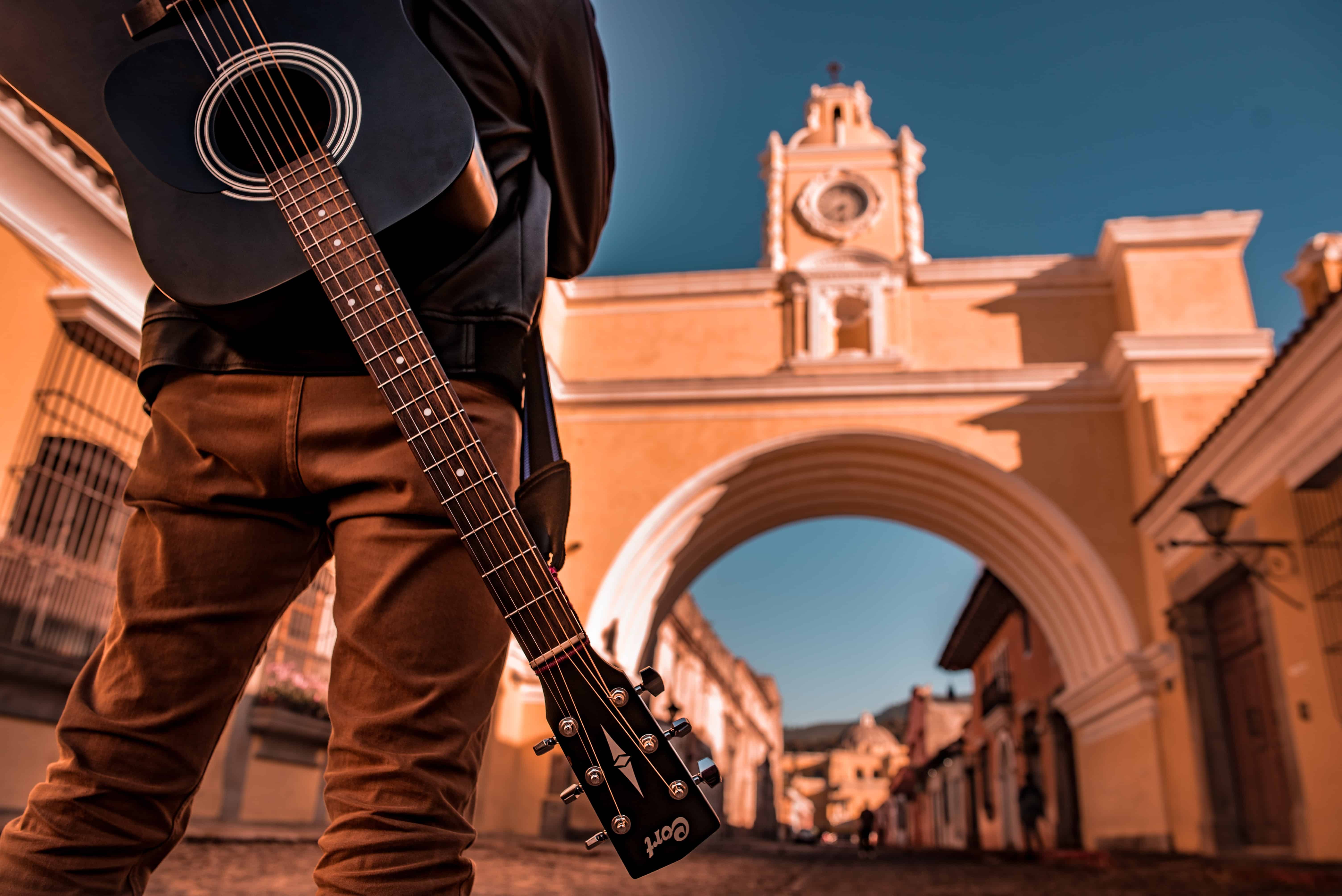Hombre de espaldas cargando una guitarra atrás con vista a la ciudad