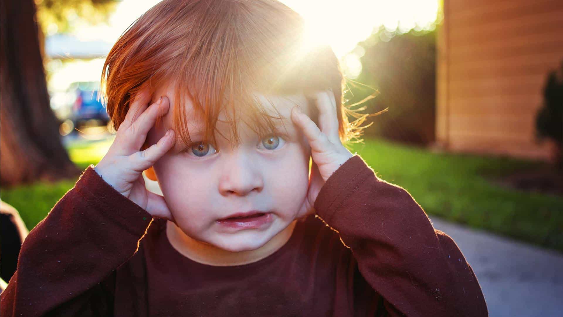 Niño viendo de frente mientras agarra su cabeza.