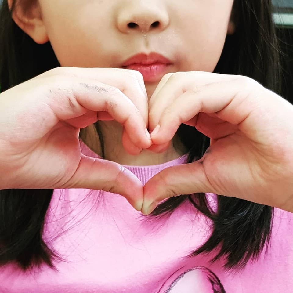 Chica coreana dibujando un corazón con sus manos.