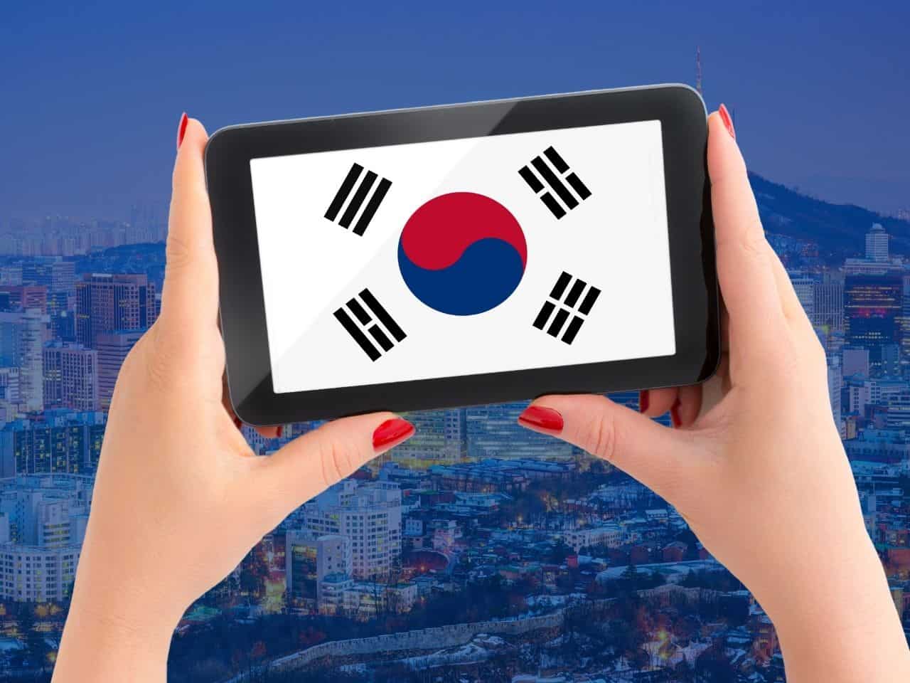 Chica sosteniendo un teléfono móvil en sus manos el cual tiene la imagen de la bandera de Corea.
