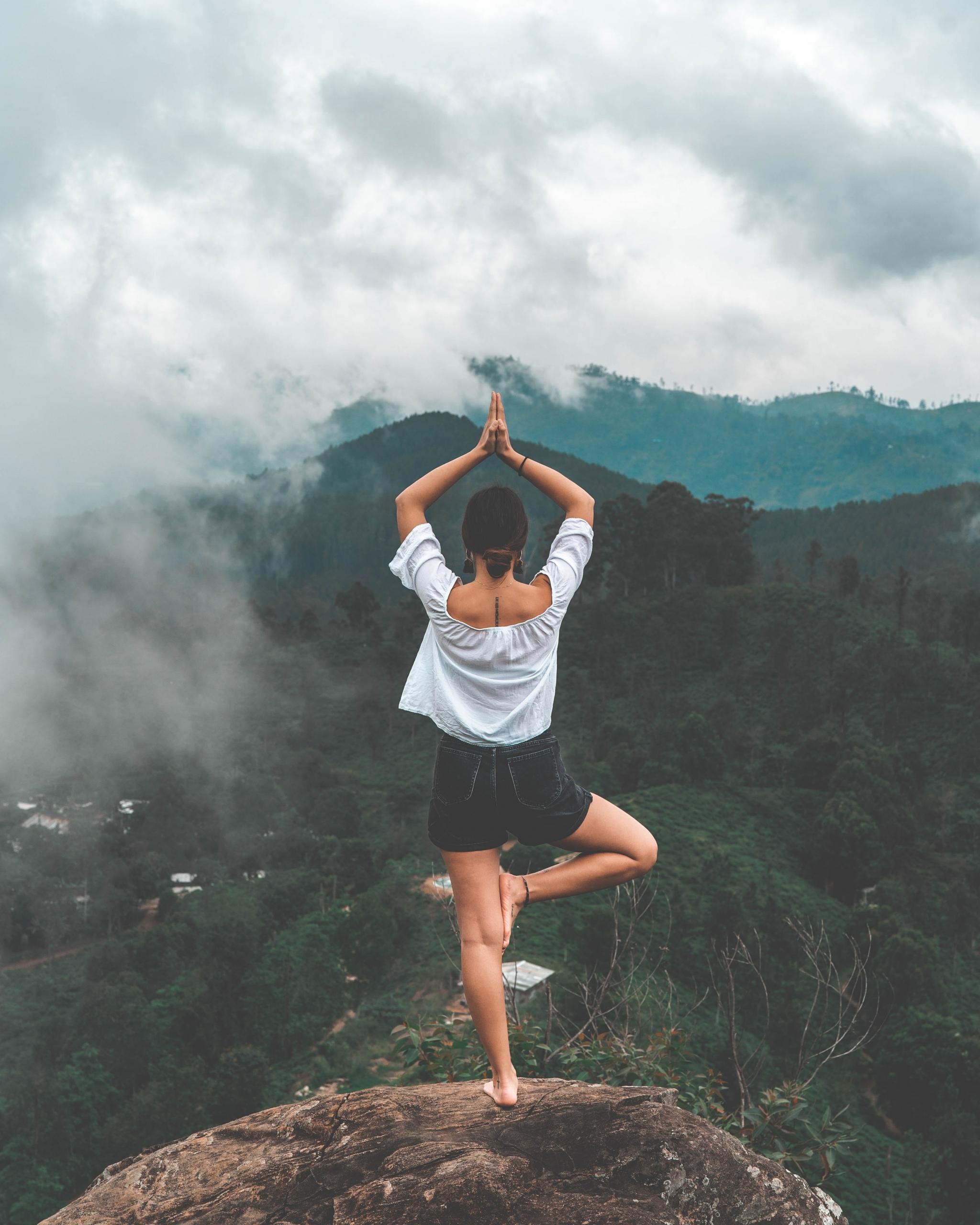 Chica realizando una asana sobre una piedra frente a un bosque. Foto deYannic Läderach