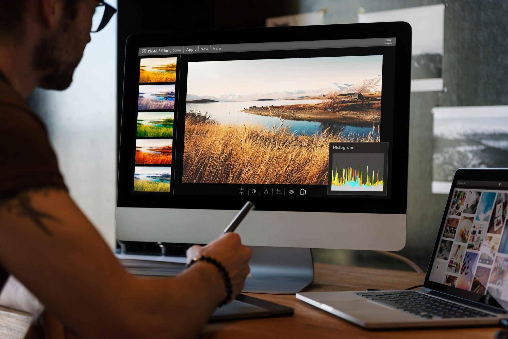 Diseñador trabajando con lápiz óptico frente a la pantalla de su iMac y la pantalla de la laptop de apoyo