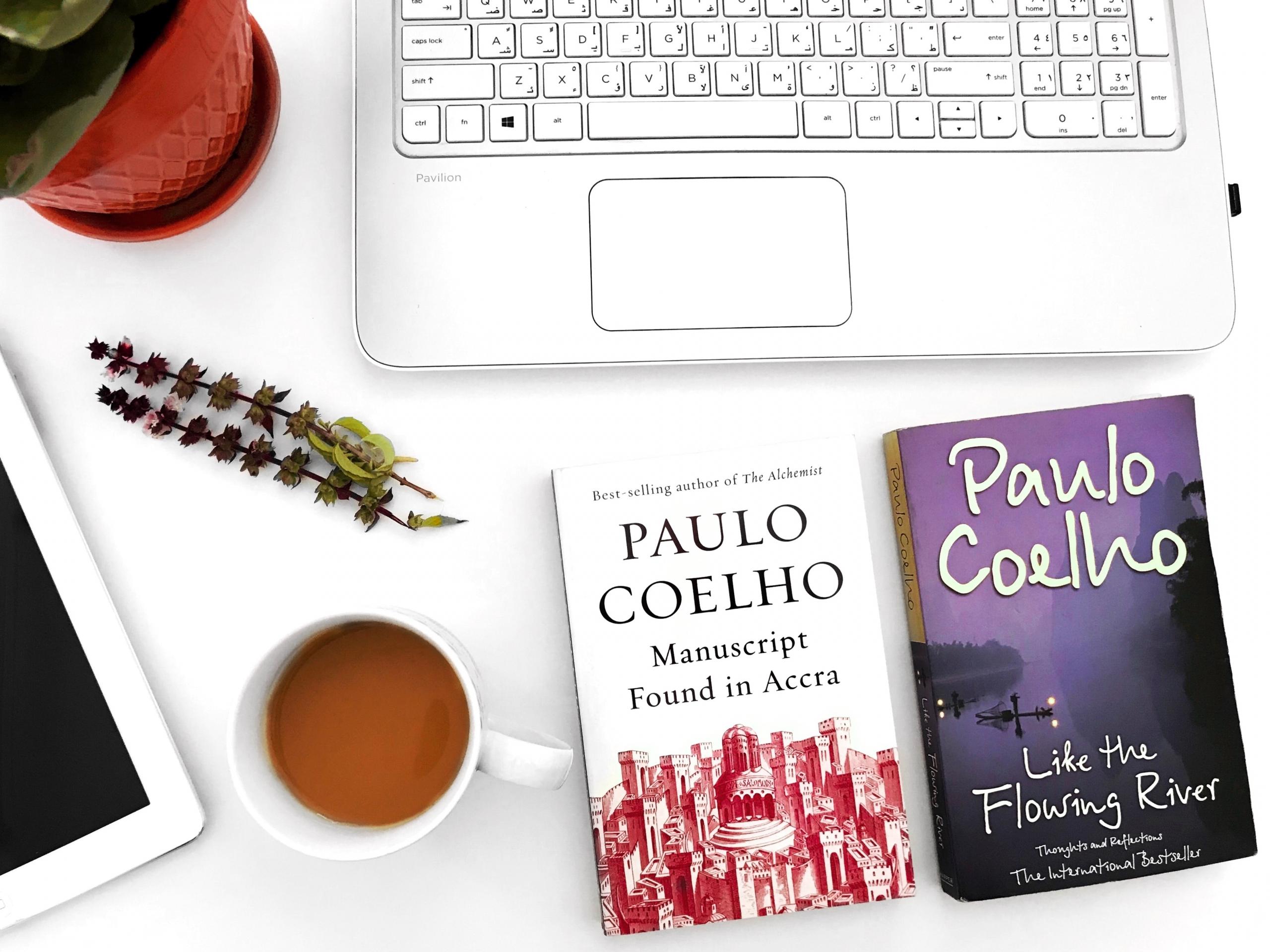 Dos libros de Paulo Coelho sobre un escritorio en donde además se ve el teclado de una laptop y una tablet