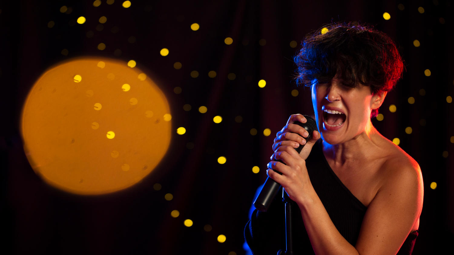 Mujer cantando en escenario oscuro con pequeñas luces