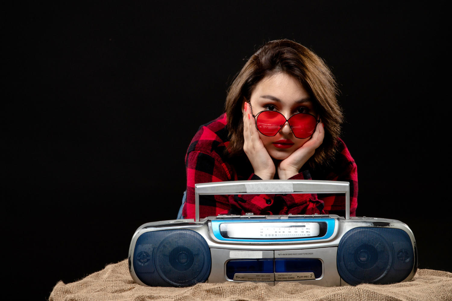 Mujer con gafas rojas frente a una grabadora mirando a la cámara