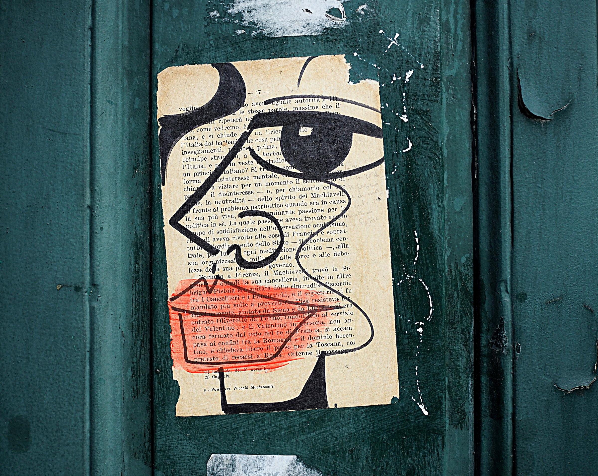 Página de un libro escrita en francés, pegada en una pared verde. Sobre la página se puede visualizar el dibujo de un rostro. Foto de Arièle Bonte