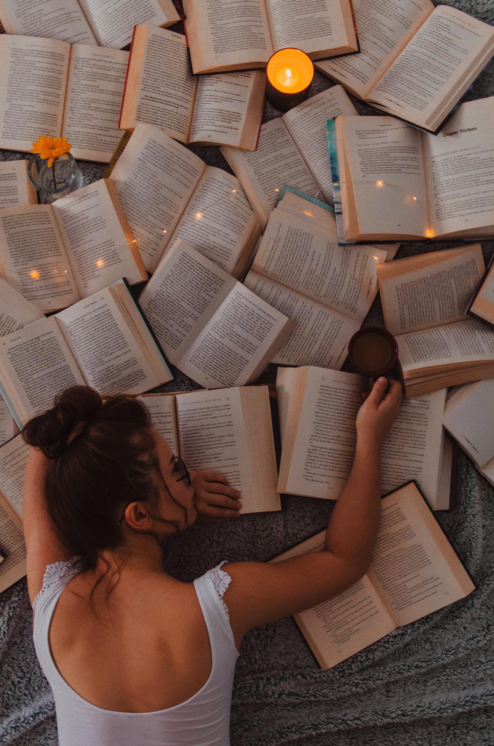 Chica Recostada junto a muchos libros abiertos.