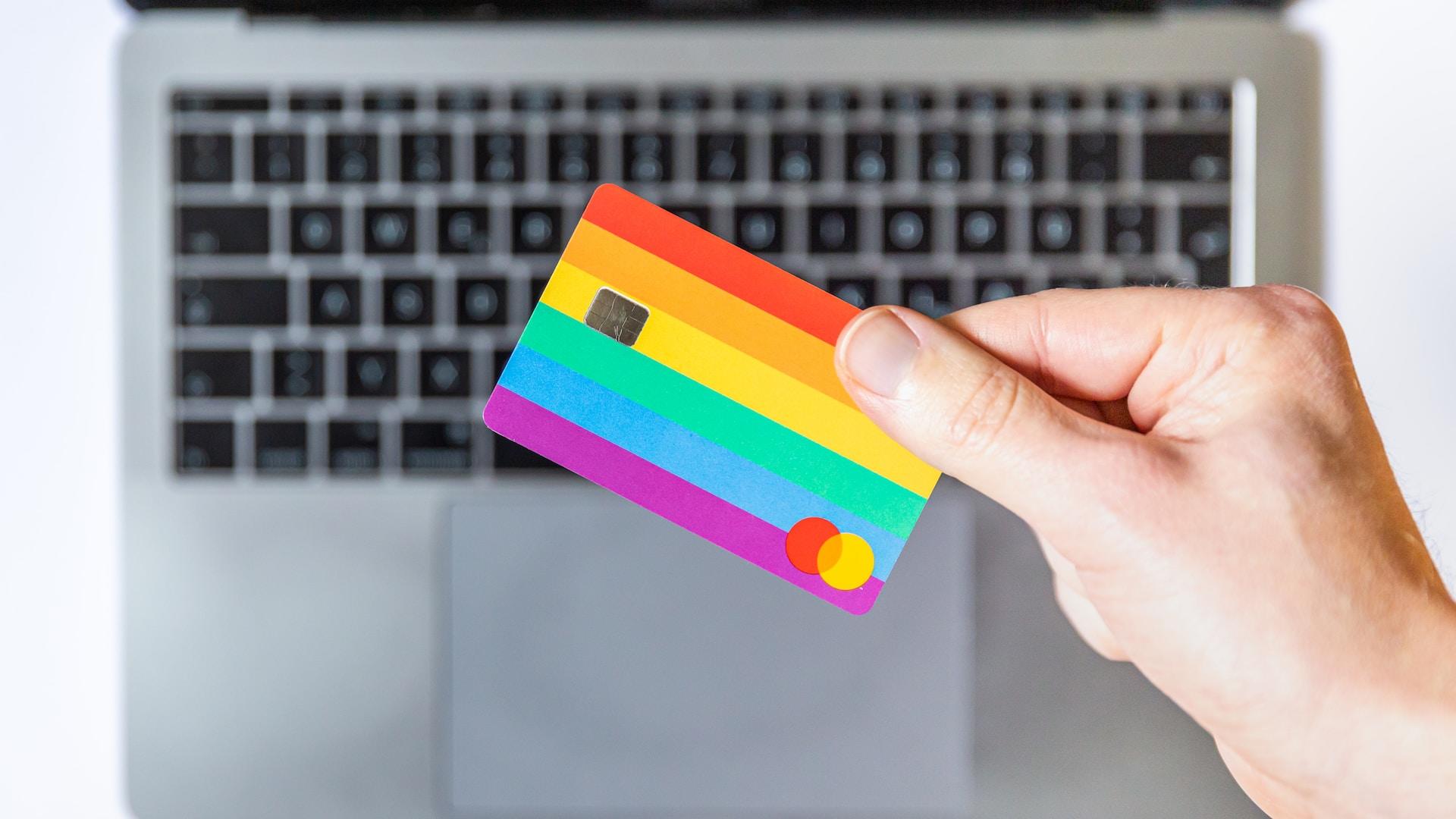 Mano sosteniendo una tarjeta bancaria de colores, sobre un teclado de un PC.