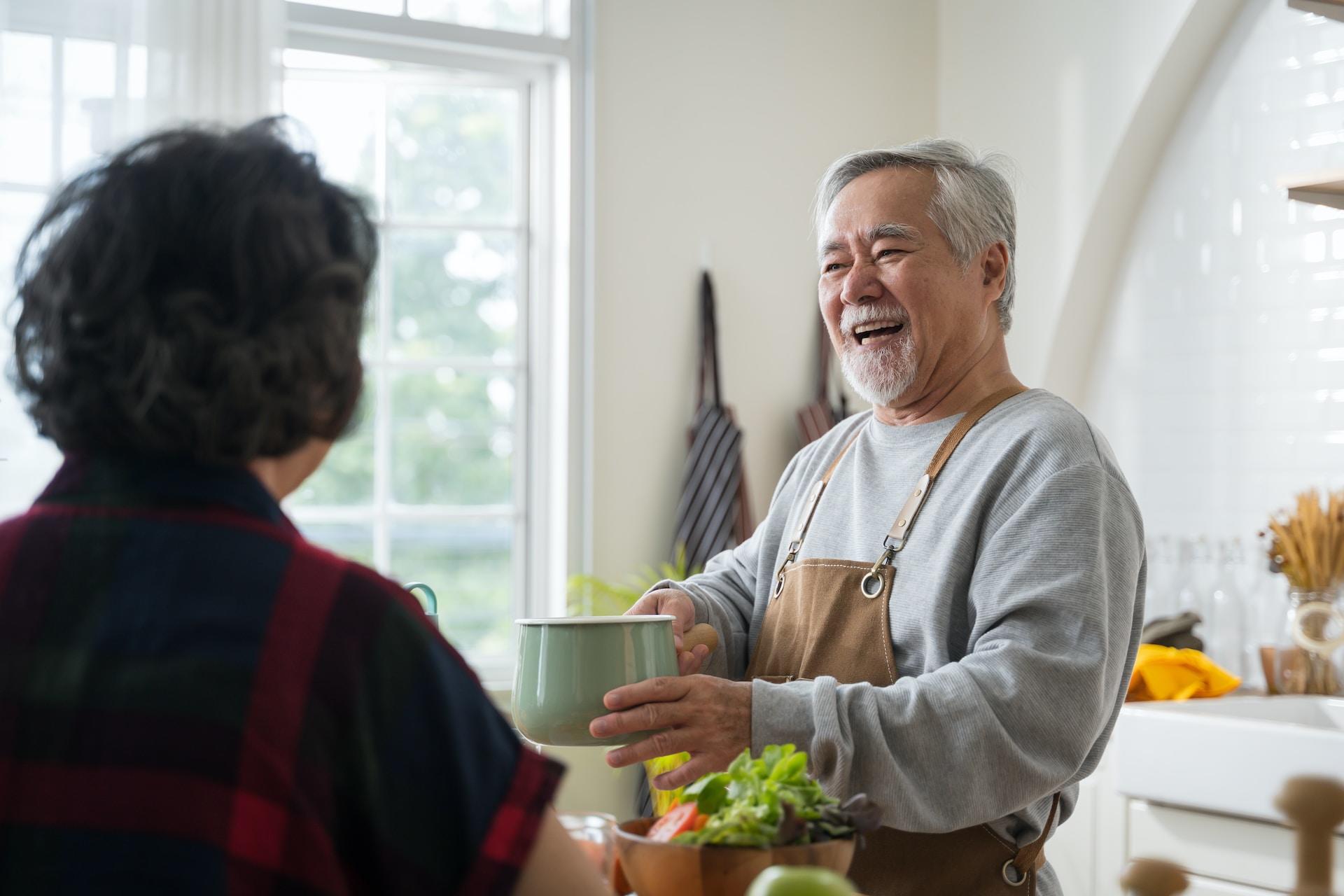 Señor mayor sonriendo mientras muestra una olla en la cocina