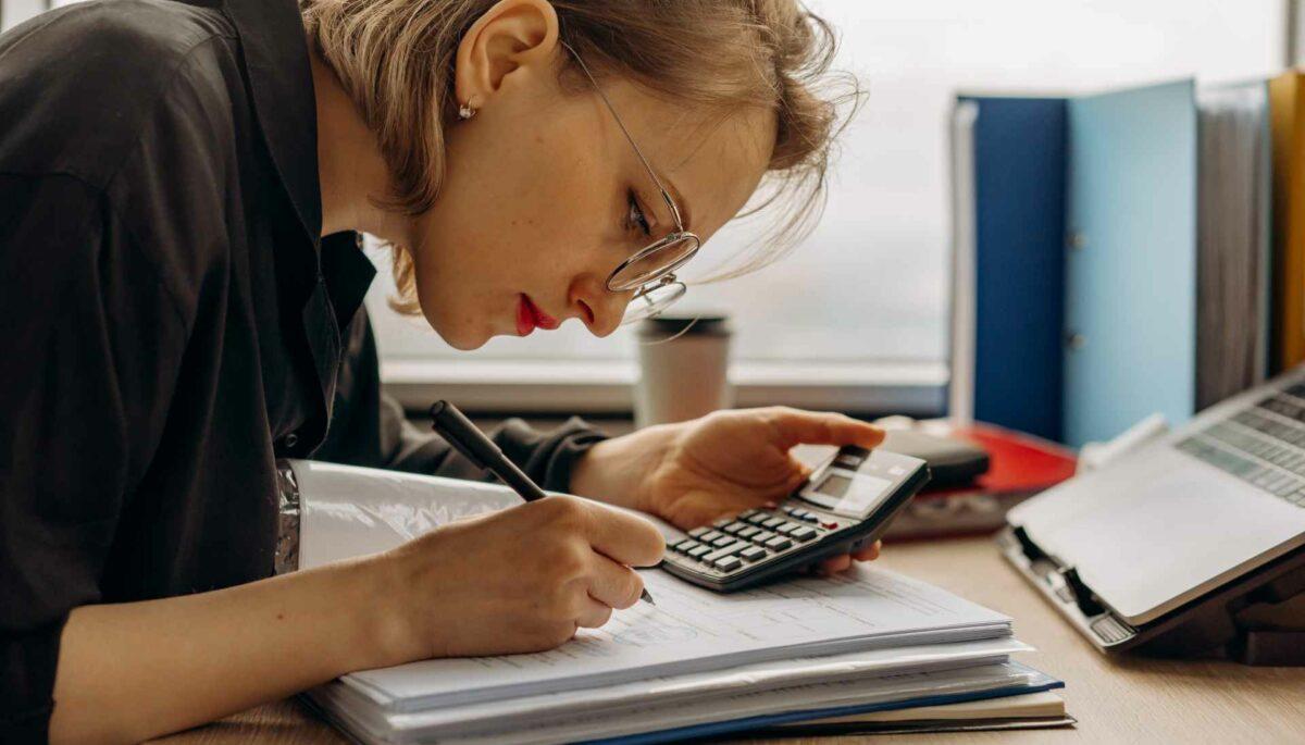 Contadora observando unas facturas mientras sostiene un lápiz en un mano y una calculadora en al otra mano.