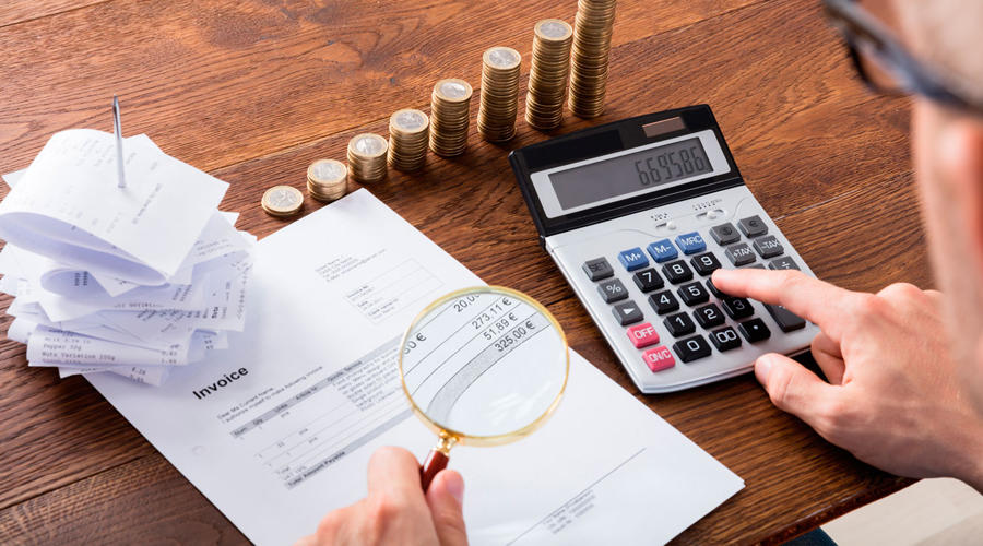 Persona usando una calculadora, una lupa, hojas y monedas.