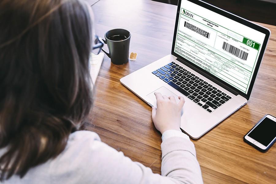 Chica con un computador portátil, el cual muestra un formulario de la DIAN.