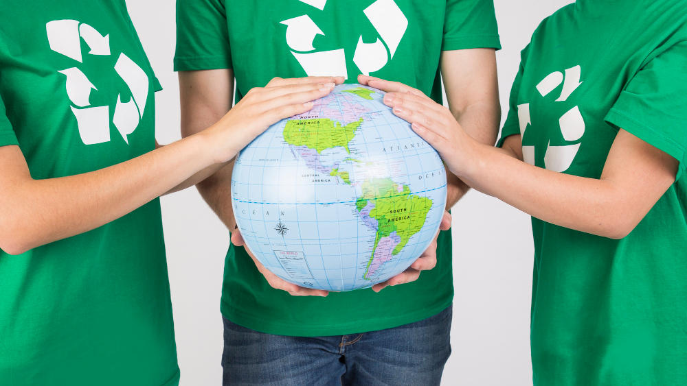 Tres personas con camiseta verde tomando un mapamundi