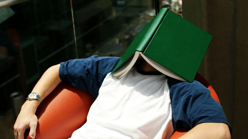 Hombre recostado de espalda en una silla con un libro cubriendo su rostro.