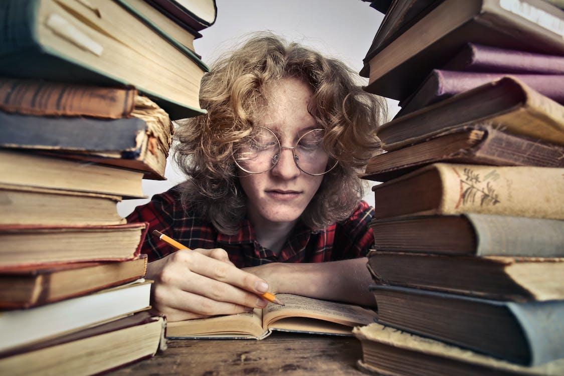 Chico junto a dos pilas de libros leyendo.