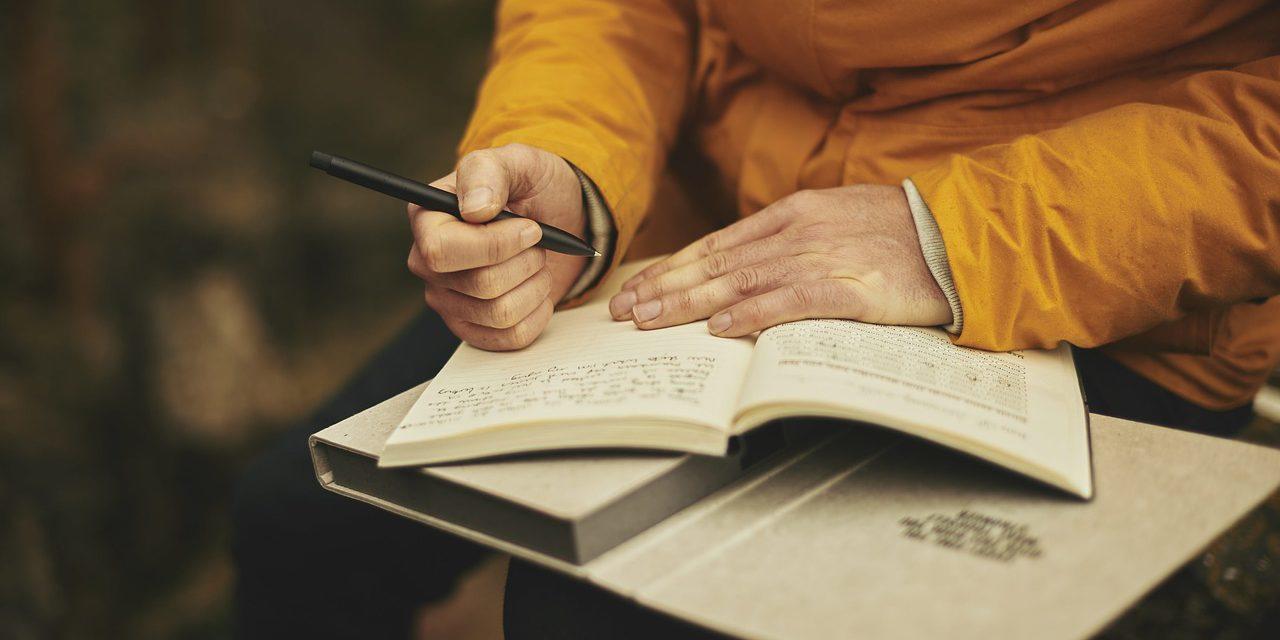 Persona vestida de amarillo sosteniendo un lápiz para escribir en un cuaderno.