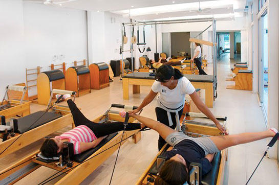 Dos chicas relaizando pilates reformer en asesoría de una instructora.