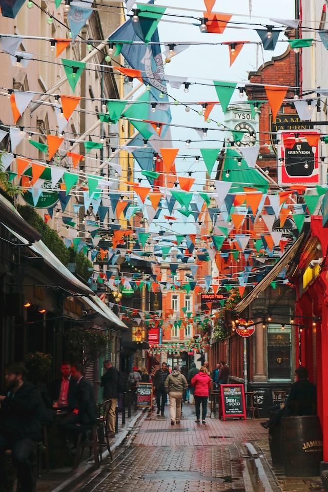 Calle de Irlanda con personas transitando y arreglos colgantes con los colores de la bandera; verde, blanco y naranja 