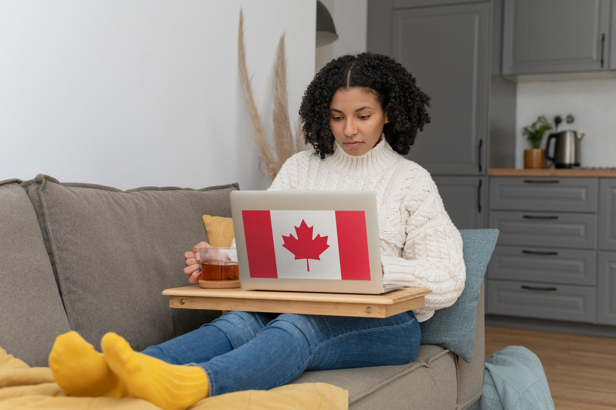 Mujer en sofá trabajando con laptop que tiene una imágen de la bandera de Canadá
