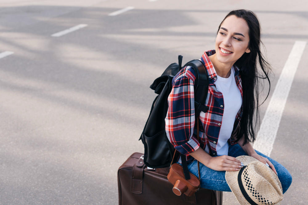 Chica sentada sobre su maleta de viaje sonriendo