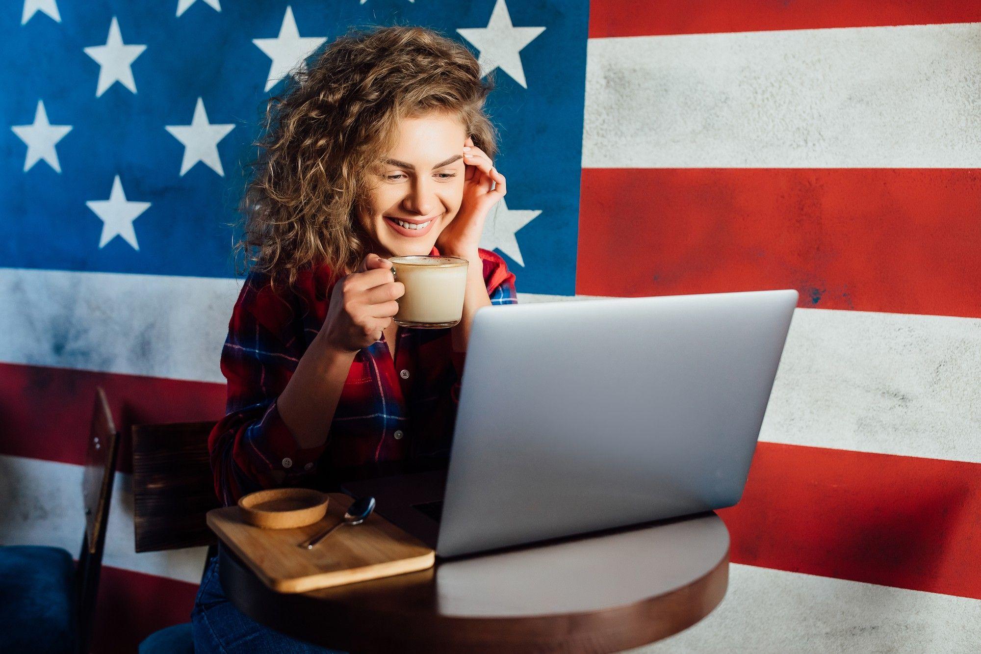 Mujer usando una laptop, de fondo la bandera de Estados Unidos
