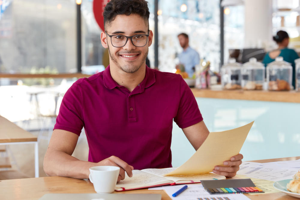 Hombre sonriente con papeles en la mano y café en la mesa