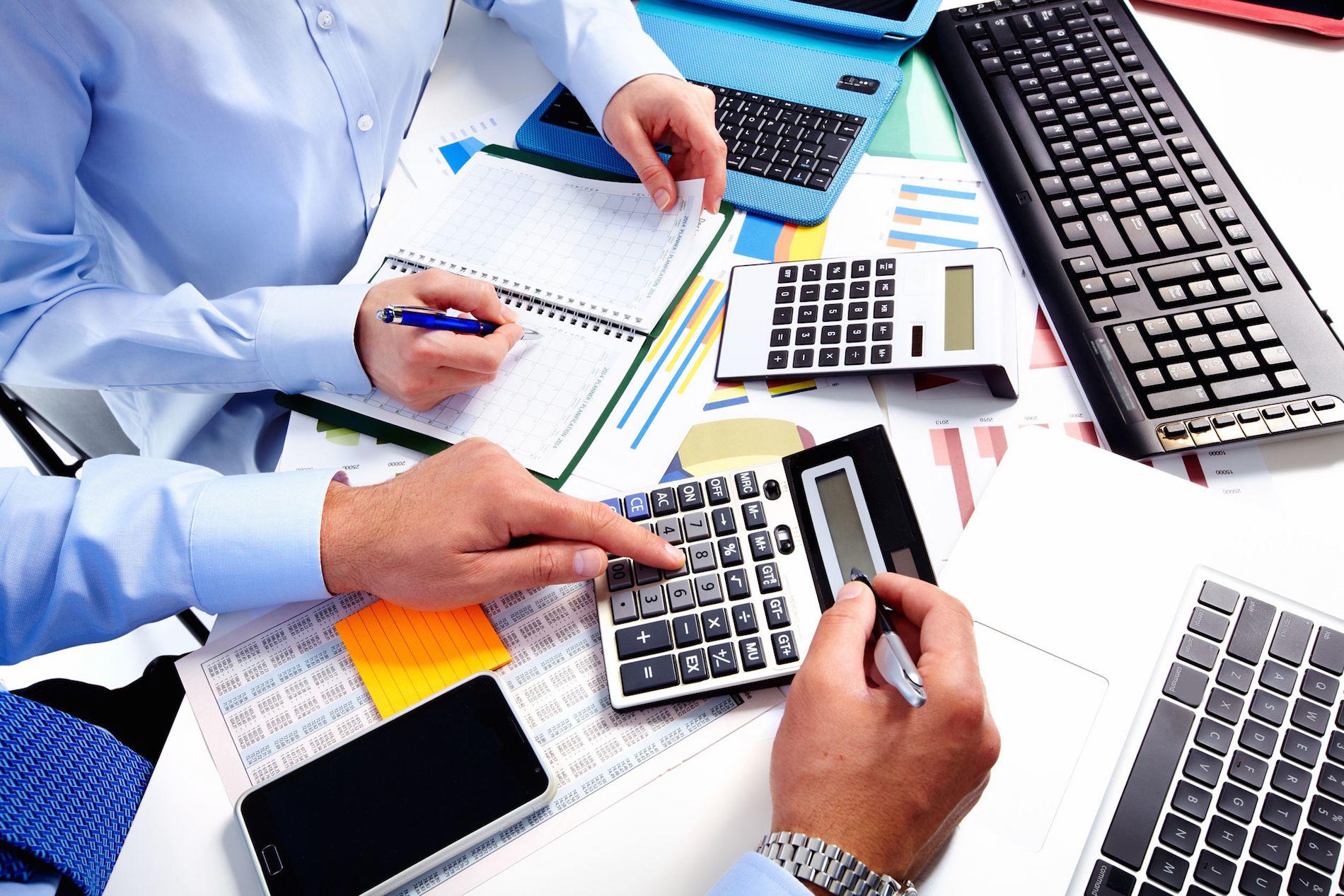 Profesor y alumno usando esferos, calculadoras y computadoras para aprender matemáticas financieras.