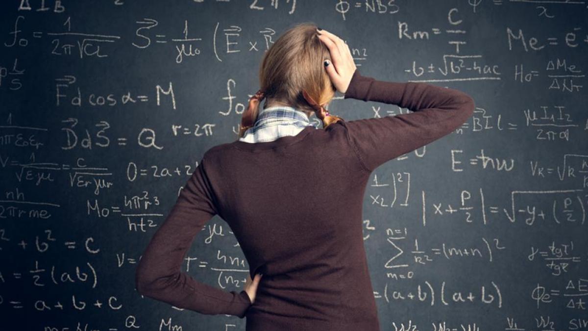 Chica observando un tablero llenos de formulas matemáticas, mientras se toca la cabeza con una mano.