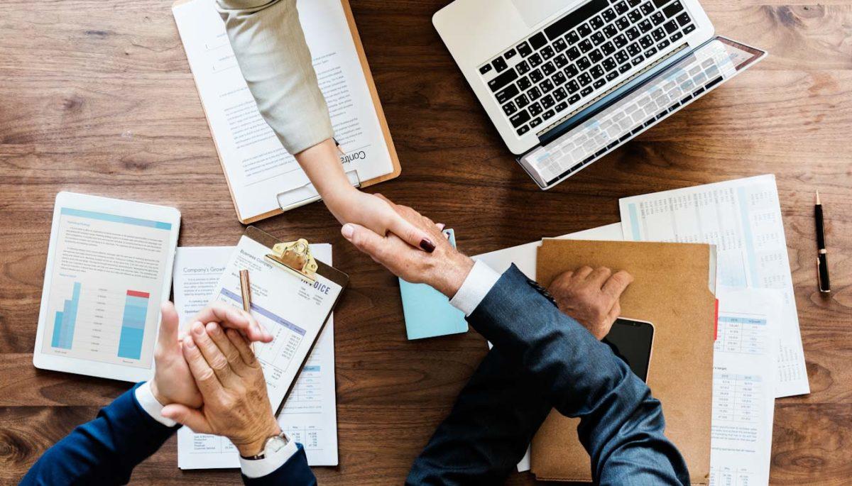 Personas estrechando las manos sobre informes financieros.