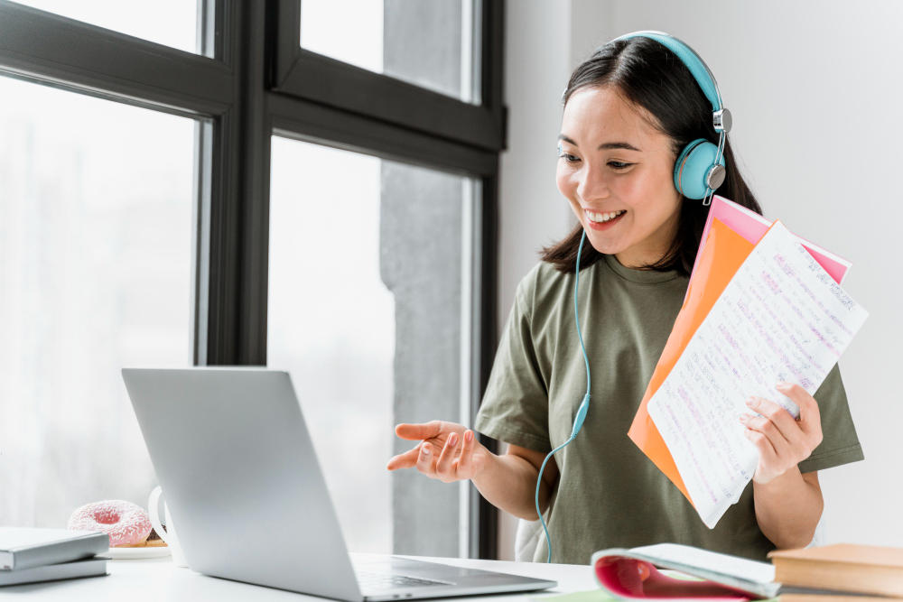 Chica estudiando en una laptop sosteniendo unos documentos
