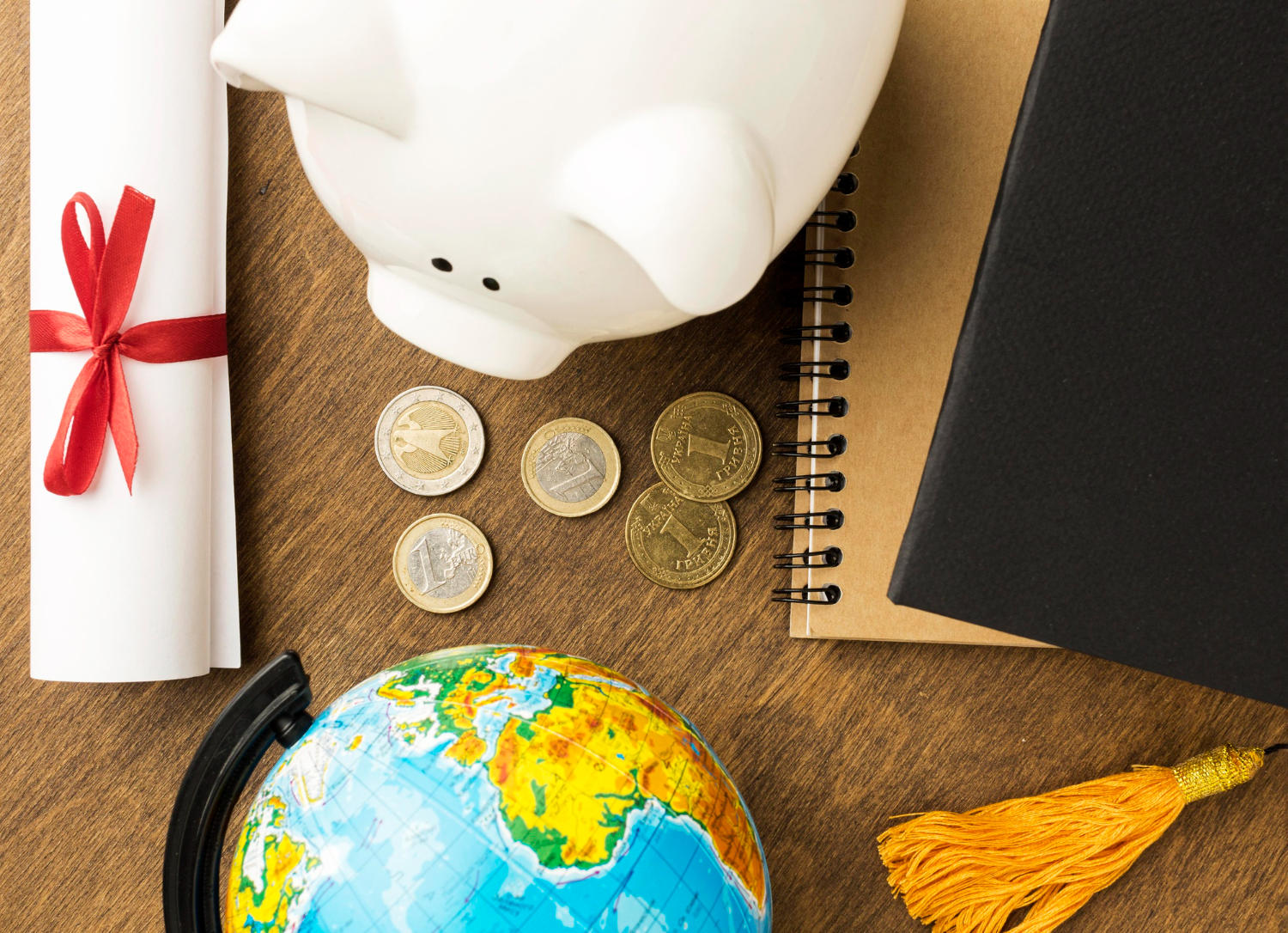 Monedas en el centro de un mapamundi un cochinito alcancía, un libro y un diploma