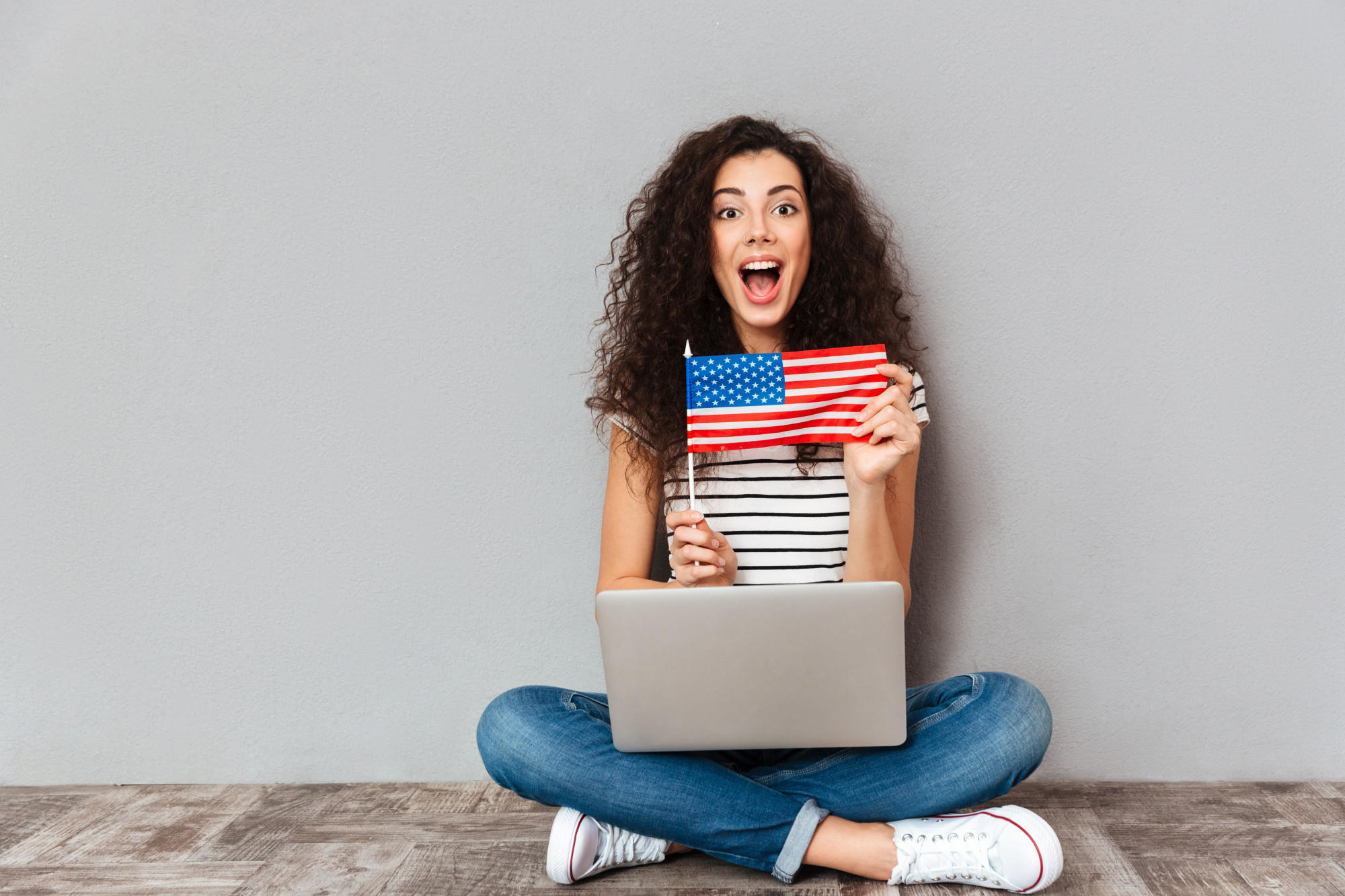 Mujer con laptop en las piernas sonriendo mientras sostiene una bandera Americana