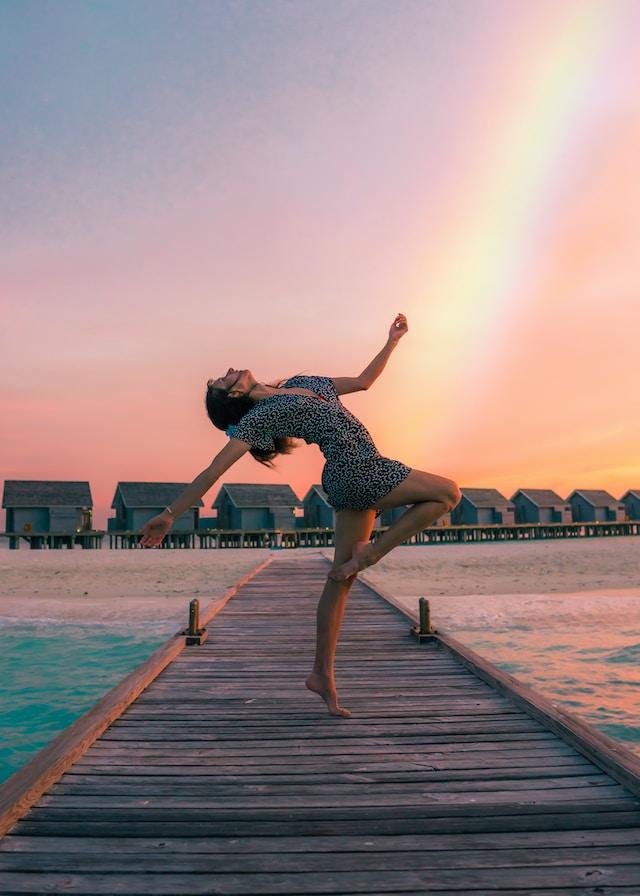 Mujer bailando en puente de un lago, al fondo se ve el arco iris