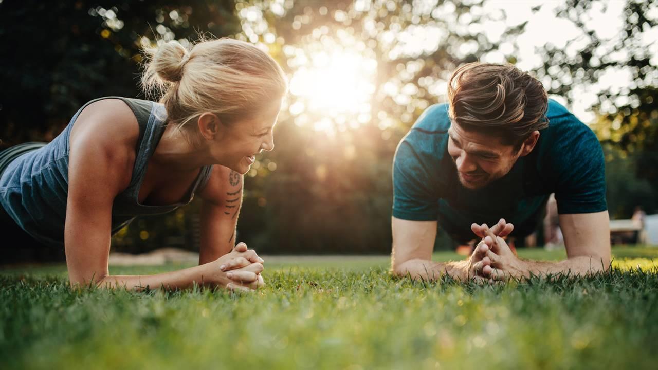 Pareja haciendo planchas de abdomen al aire libre mientras sonríen.