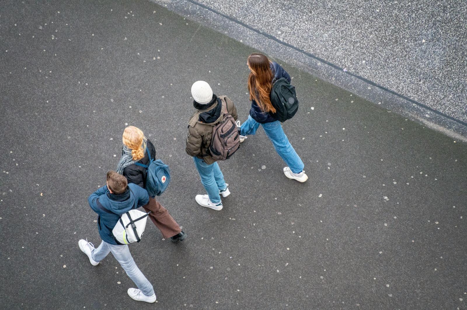 Cuatro estudiantes caminando juntos por una calle urbana, vistos desde una perspectiva aérea.