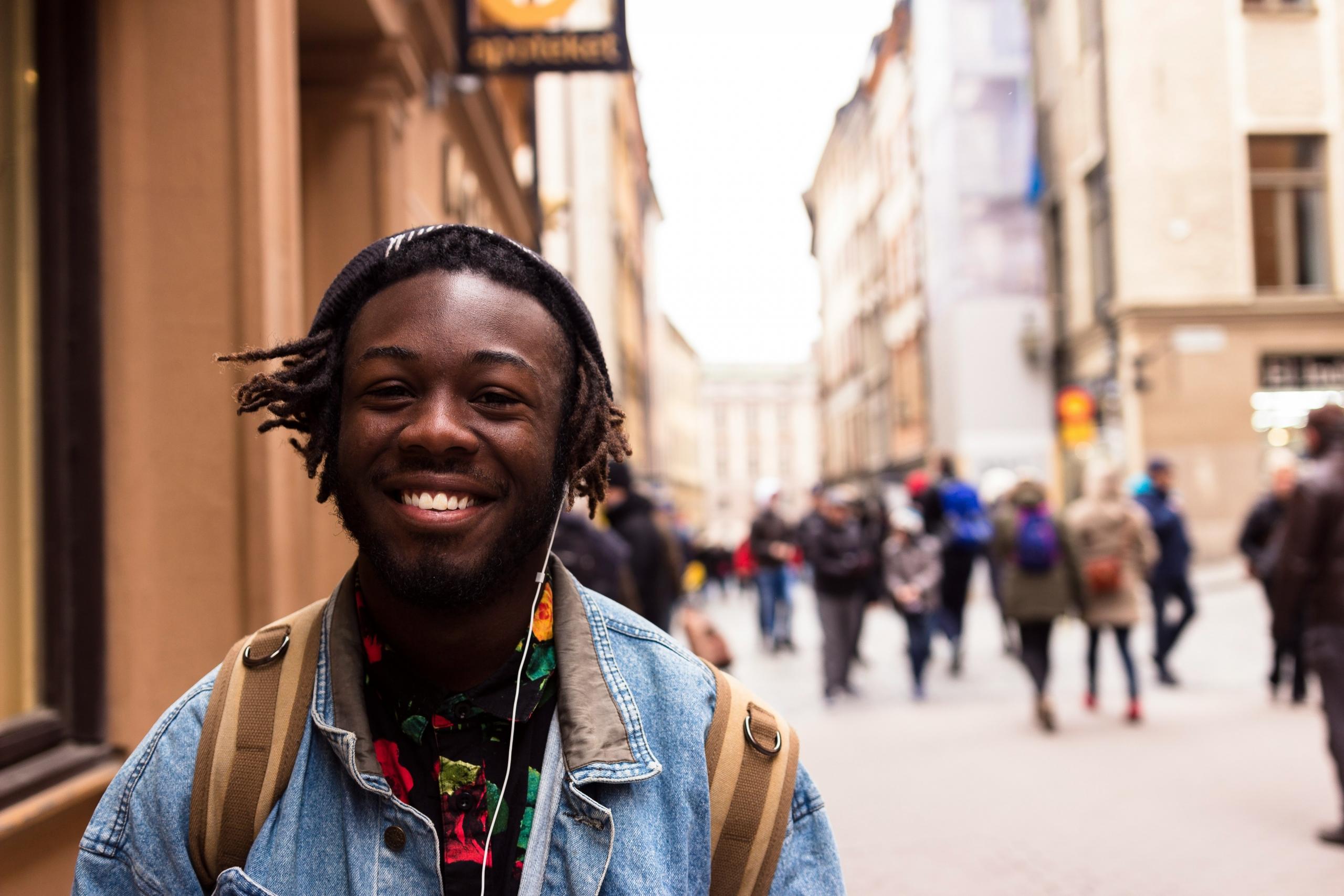 Imagen de estudiante sonriendo, con audifonos y con una mochila caminando por la ciudad