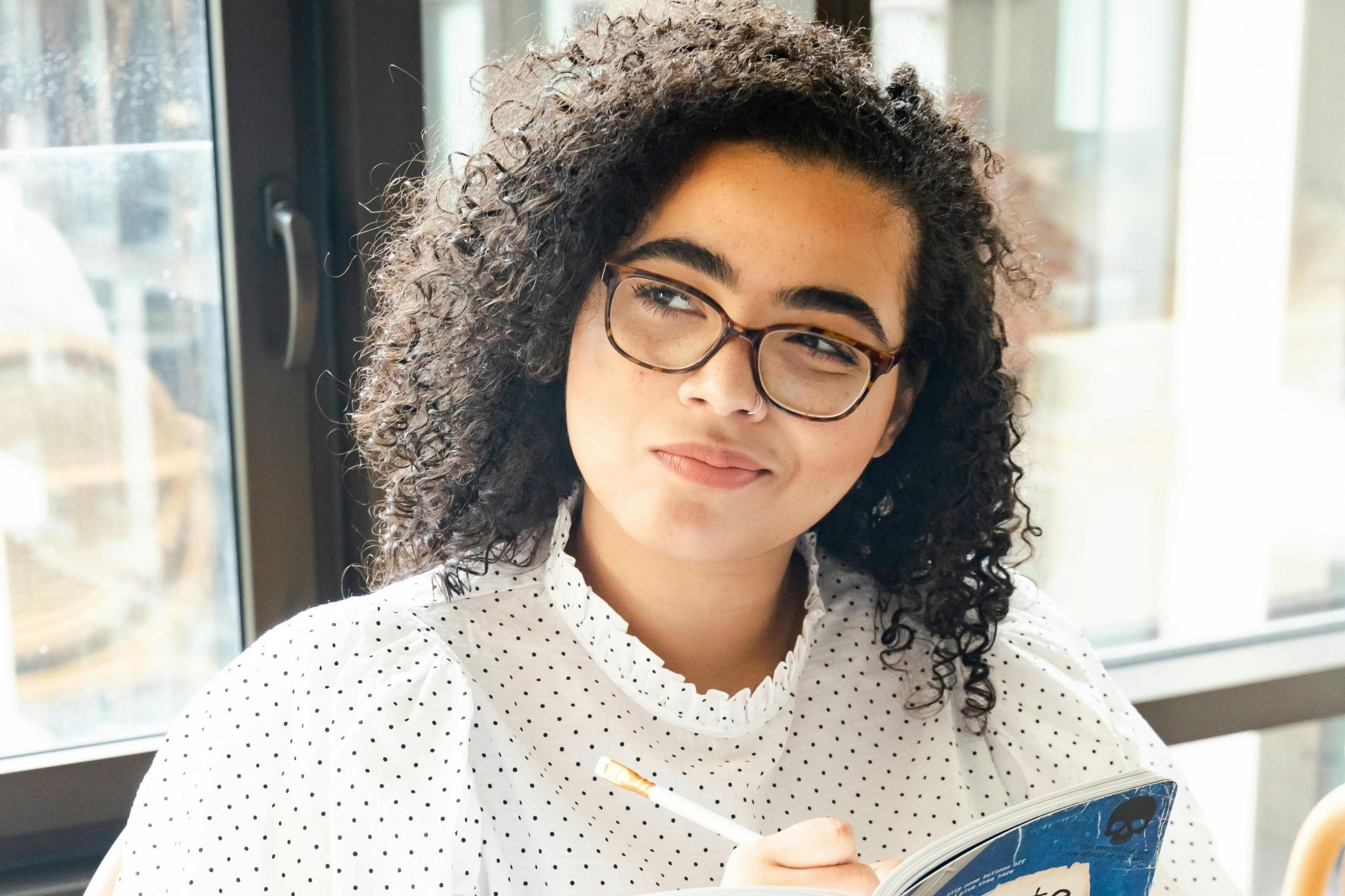 Mujer en camisa de lunares blancos y negros escriendo en un libro azul y blanco