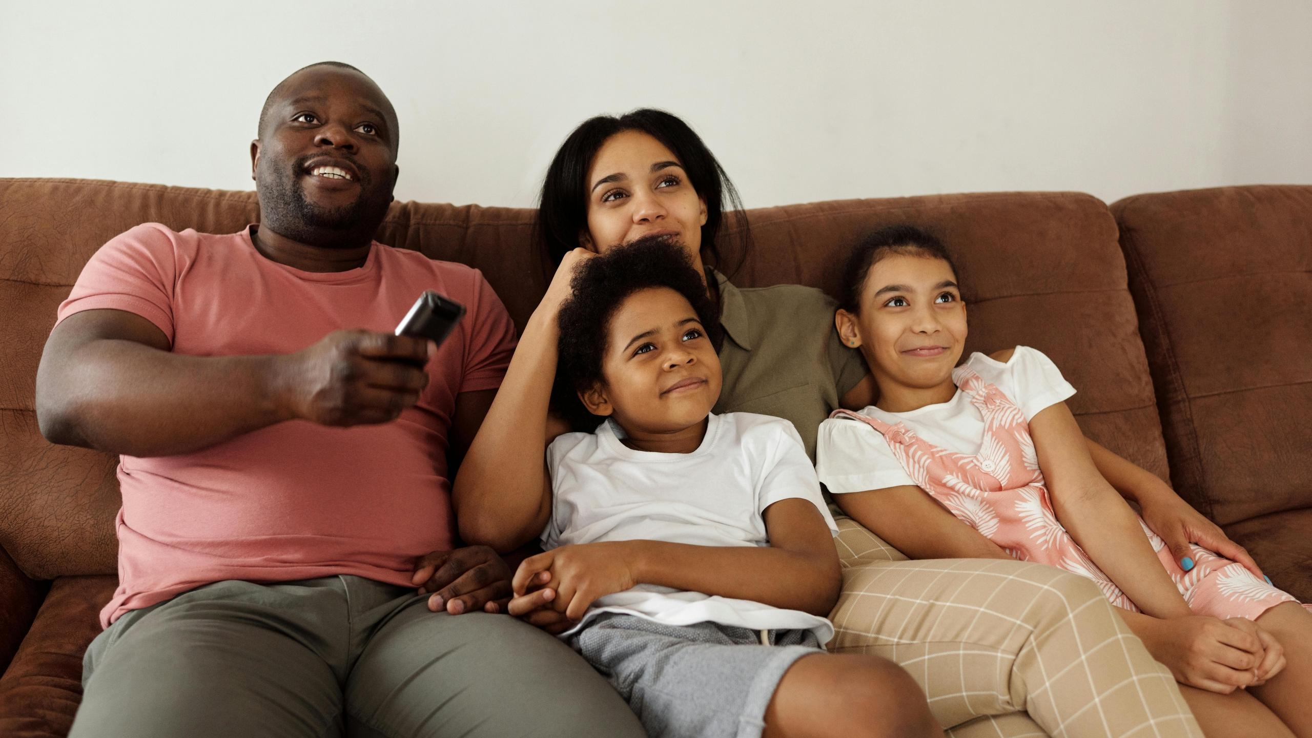 Imagen de una familia sentada en el sofá con un control remoto para ver los juegos olímpicos desde casa 