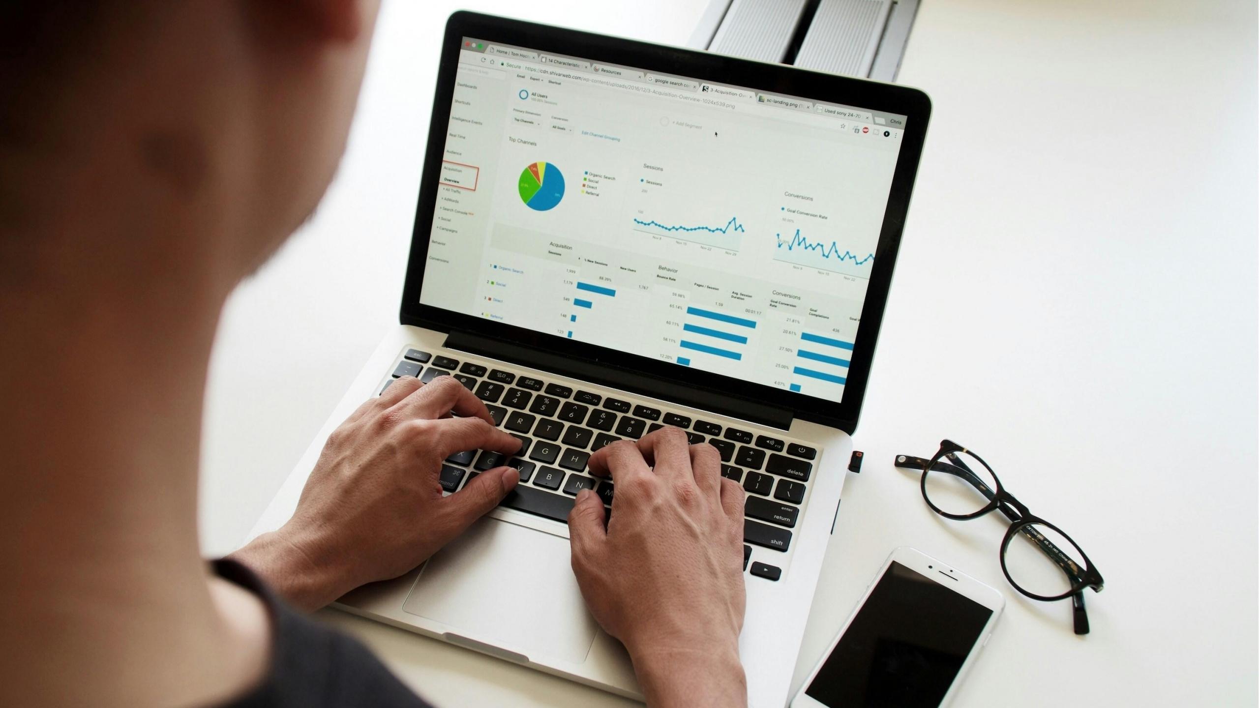 Persona escribiendo sobre su computador mientras visualiza un gráfico que muestra datos de excel