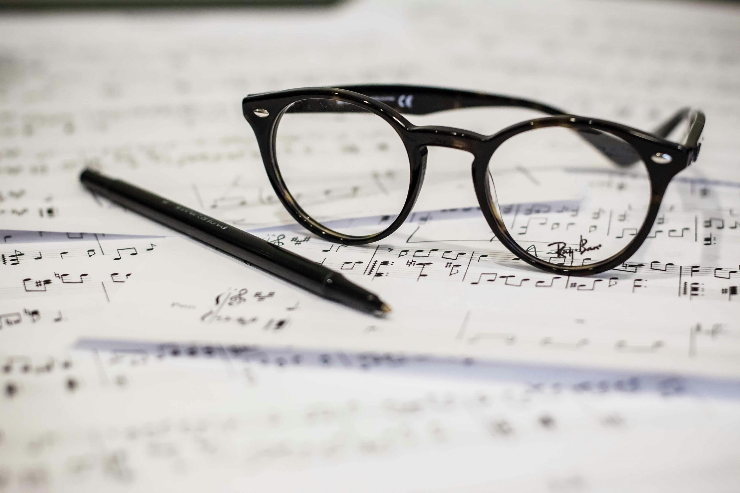 Gafas y lapcero sobre una hoja de solfeo de una armonia musical.